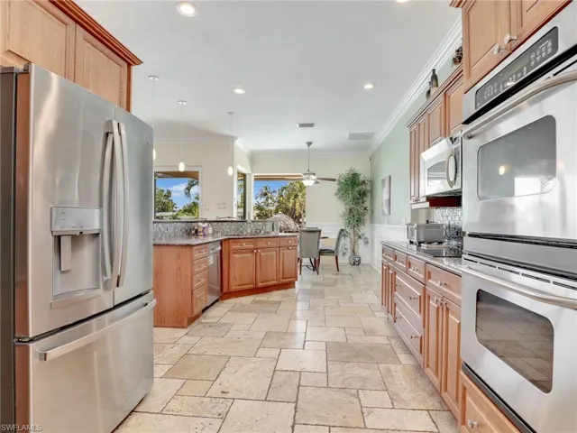 Kitchen with ornamental molding, appliances with stainless steel finishes, decorative light fixtures, ceiling fan, and light tile floors