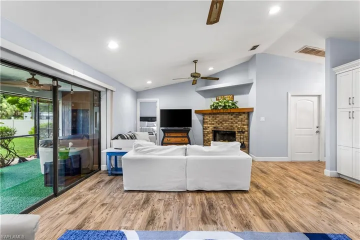 Living room with light hardwood / wood-style flooring, a fireplace, lofted ceiling, and ceiling fan