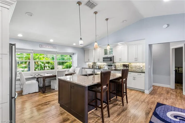 Kitchen with stainless steel appliances, hanging light fixtures, an island with sink, sink, and light wood-style flooring
