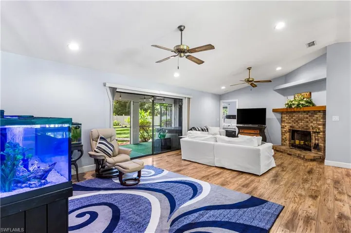 Living room featuring a brick fireplace, ceiling fan, wood-type flooring, and vaulted ceiling