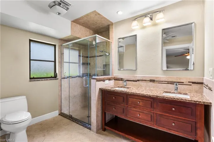 Bathroom with double vanity, a shower with shower door, toilet, ceiling fan, and tile patterned floors