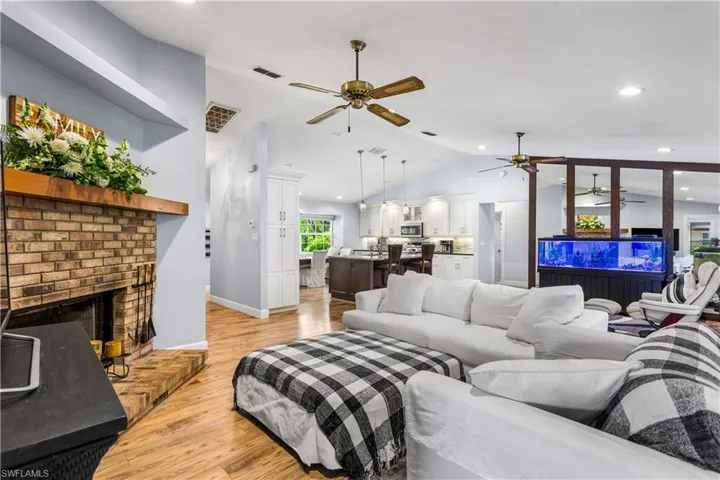 Living room with lofted ceiling, light hardwood / wood-style flooring, a brick fireplace, and ceiling fan