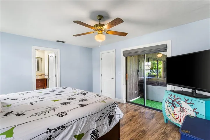 Bedroom with dark wood-type flooring, access to outside, ensuite bath, and ceiling fan