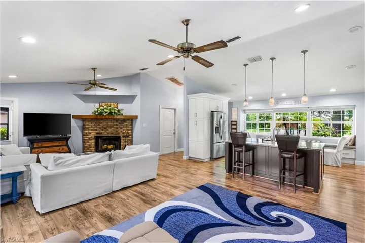 Living room featuring ceiling fan, light wood-type flooring, a brick fireplace, and high vaulted ceiling