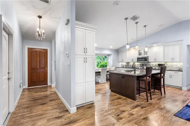 Kitchen with wood-type flooring, white cabinets, pendant lighting, an island with sink, and a breakfast bar