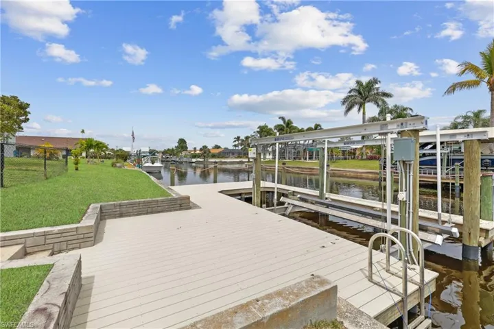 View of dock with boat lift, a water view, and fenced backyard.