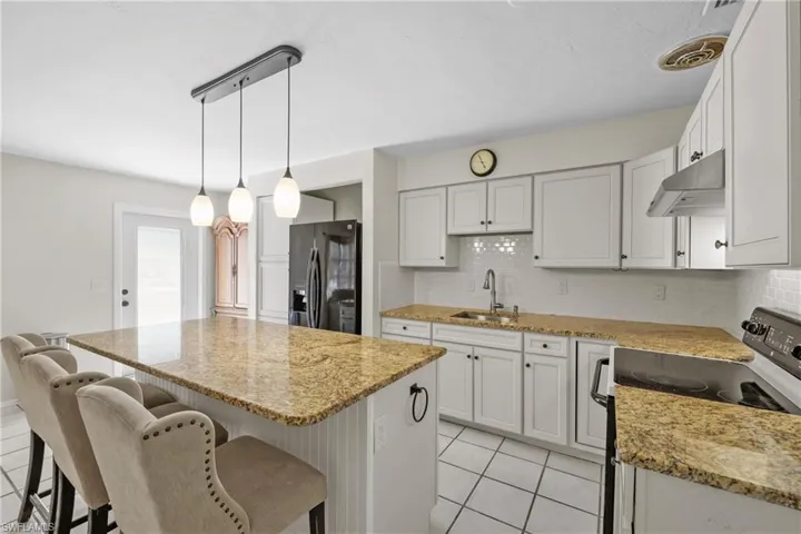 1/1 Side: Kitchen featuring a sink, electric range oven, a kitchen island, wall chimney exhaust hood, and refrigerator.