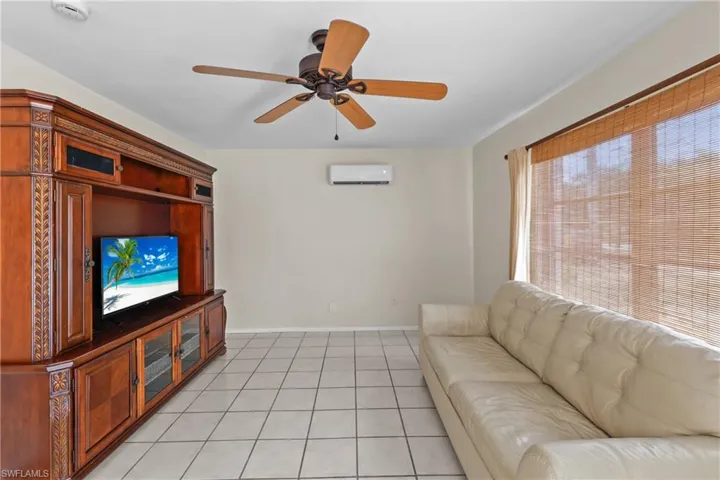 1/1 Side: Living room featuring baseboards, a wall mounted AC, ceiling fan, and light tile floors