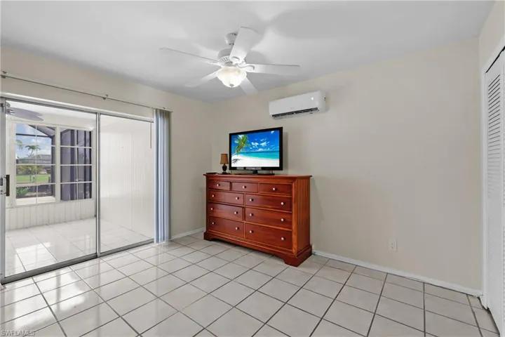 1/1 Side: Bedroom featuring a wall mounted air conditioner, light tile patterned floors, baseboards, ceiling fan, and a closet