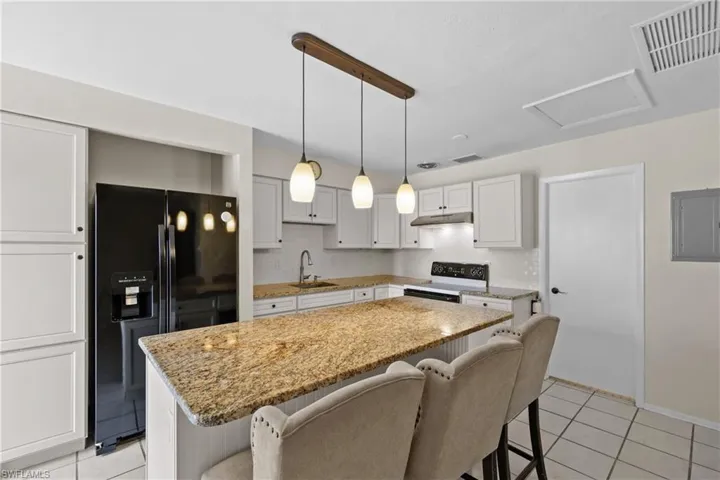 Kitchen with black refrigerator with ice dispenser, under cabinet range hood, electric range, a sink