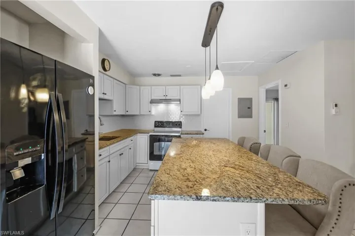 Kitchen featuring a kitchen island, under cabinet range hood, refrigerator with ice dispenser, white cabinetry and granite countertops.
