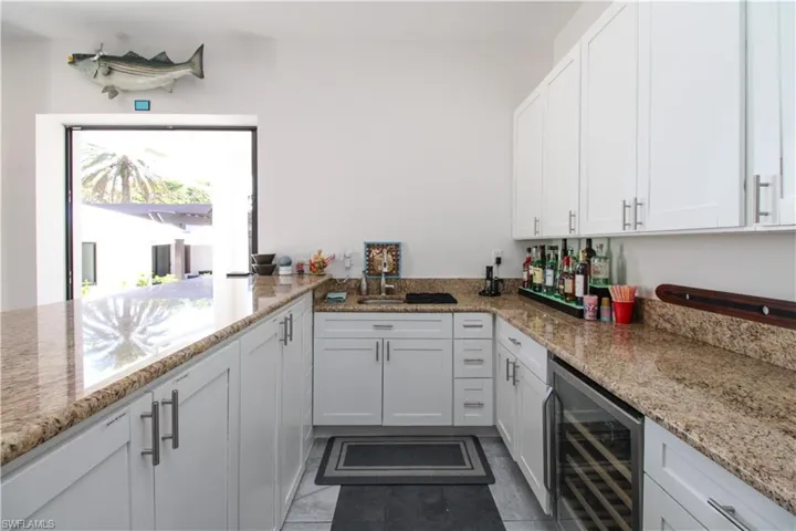 Kitchen with light stone countertops, dark tile patterned flooring, white cabinetry, and beverage cooler