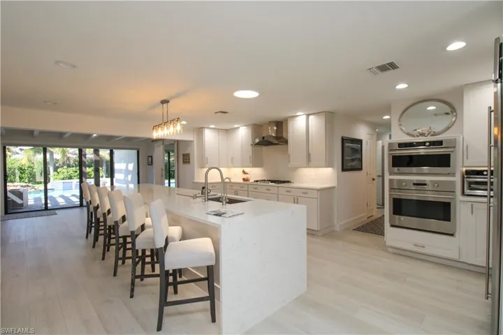 Kitchen with sink, wall chimney range hood, gas cooktop, decorative light fixtures, and a kitchen island with sink
