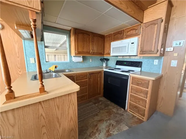 Kitchen featuring electric stove, light countertops, white microwave, brown cabinetry, and a drop ceiling