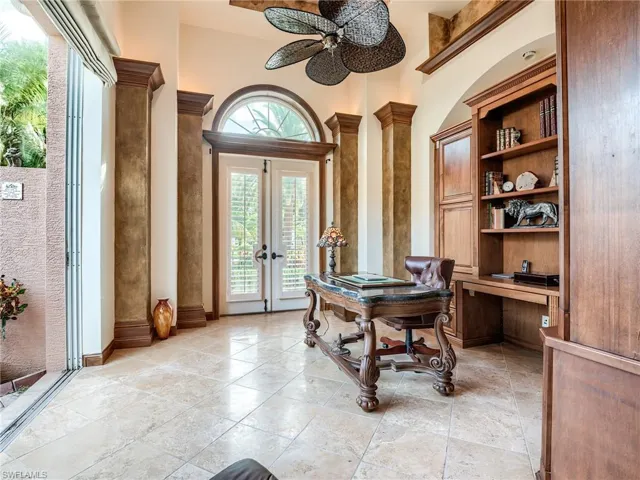 Tiled home office featuring decorative columns, ceiling fan, french doors, and a high ceiling