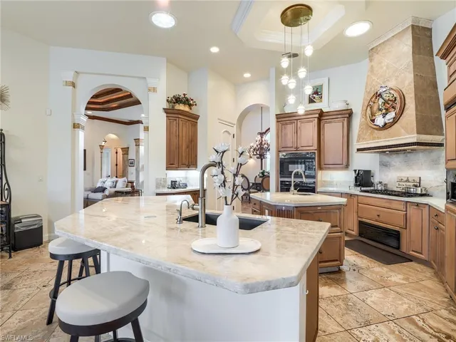 Kitchen featuring a kitchen bar, a raised ceiling, ornamental molding, custom range hood, and an island with sink