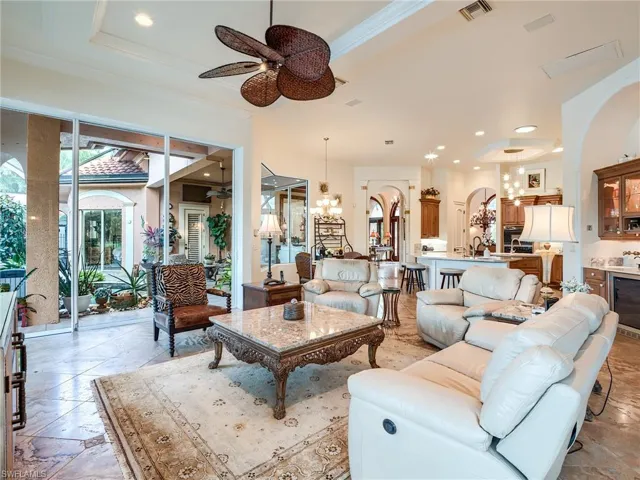 Tiled living room with sink, a raised ceiling, and ceiling fan with notable chandelier
