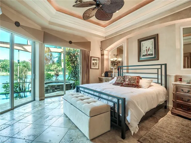 Tiled bedroom with access to outside, ceiling fan with notable chandelier, a raised ceiling, and multiple windows