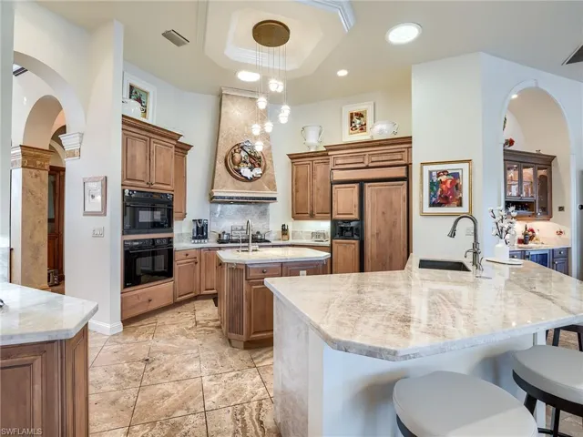 Kitchen with black double oven, premium range hood, an island with sink, sink, and a tray ceiling