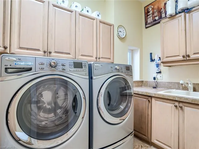 Laundry area featuring separate washer and dryer, cabinets, and sink