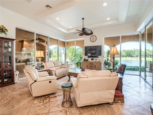 Tiled living room with ceiling fan, ornamental molding, and a tray ceiling