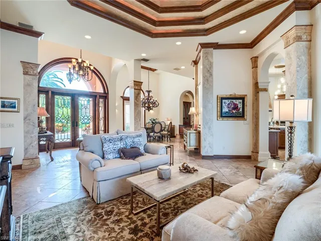 Living room with decorative columns, crown molding, a chandelier, a tray ceiling, and light tile patterned floors