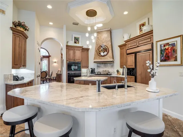 Kitchen featuring hanging light fixtures, premium range hood, decorative backsplash, sink, and a spacious island
