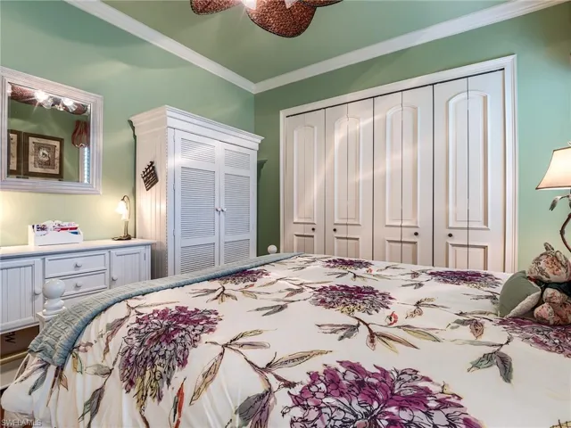 Bedroom with ceiling fan, multiple closets, and ornamental molding