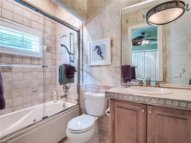 Full bathroom featuring toilet, tile patterned floors, vanity, bath / shower combo with glass door, and ceiling fan