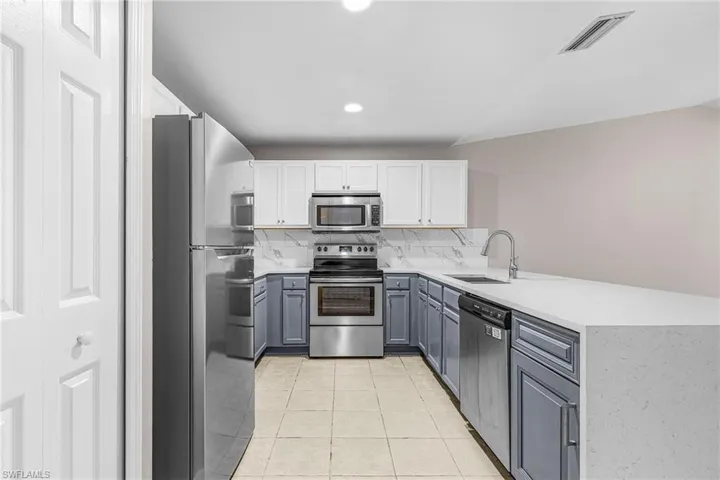 Kitchen featuring white cabinetry, appliances with stainless steel finishes, a peninsula, light stone countertops, and light tile patterned floors