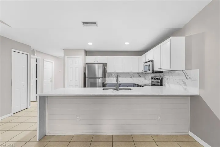 Kitchen with a peninsula, tasteful backsplash, stainless steel appliances, white cabinetry, and light stone counters