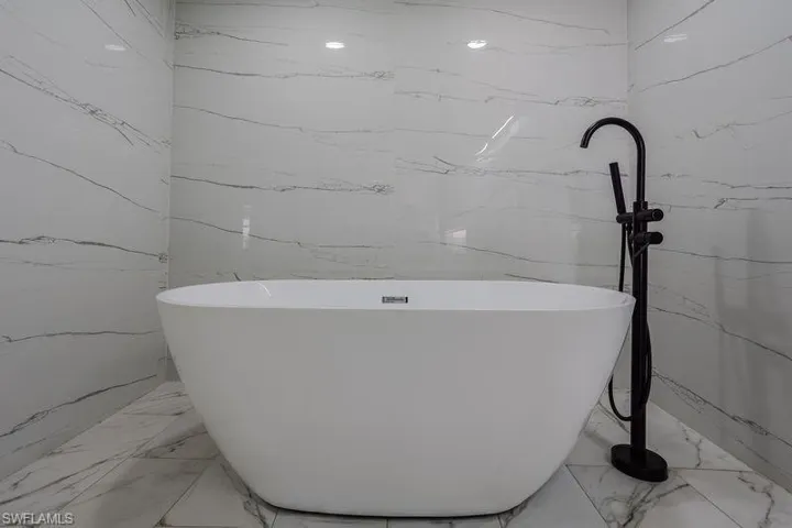 Full bathroom featuring light marble finish flooring and a freestanding tub