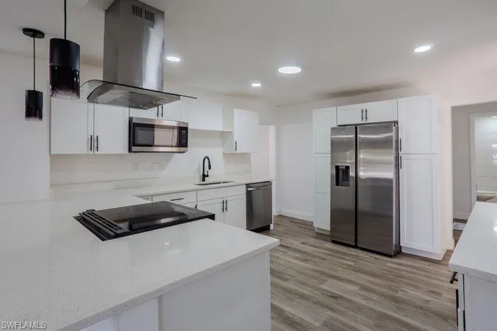 Kitchen with stainless steel appliances, island exhaust hood, white cabinetry, light stone counters, and recessed lighting