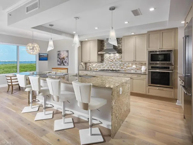 Kitchen with a center island with sink, light wood-type flooring, built in appliances, sink, and wall chimney exhaust hood