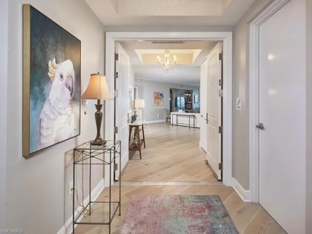 Hall with light hardwood / wood-style floors, an inviting chandelier, and a tray ceiling