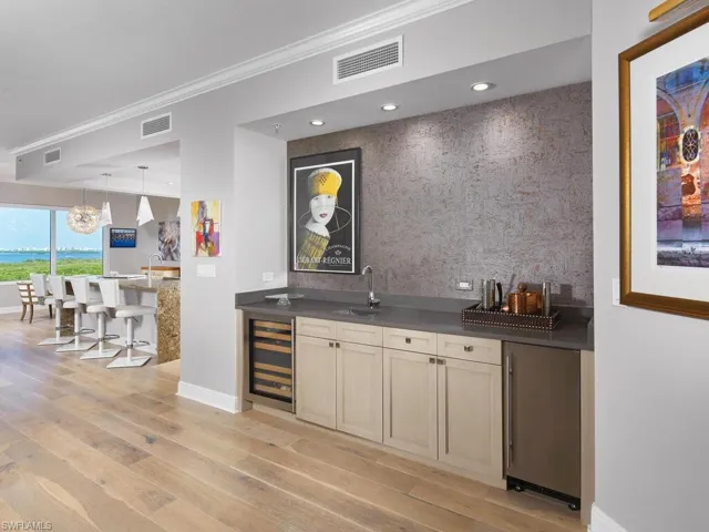 Bar with light hardwood / wood-style floors, sink, wine cooler, crown molding, and stainless steel fridge