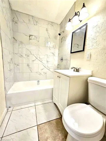 Full bathroom featuring vanity, light marble finish floors, shower / tub combination, and a textured wall