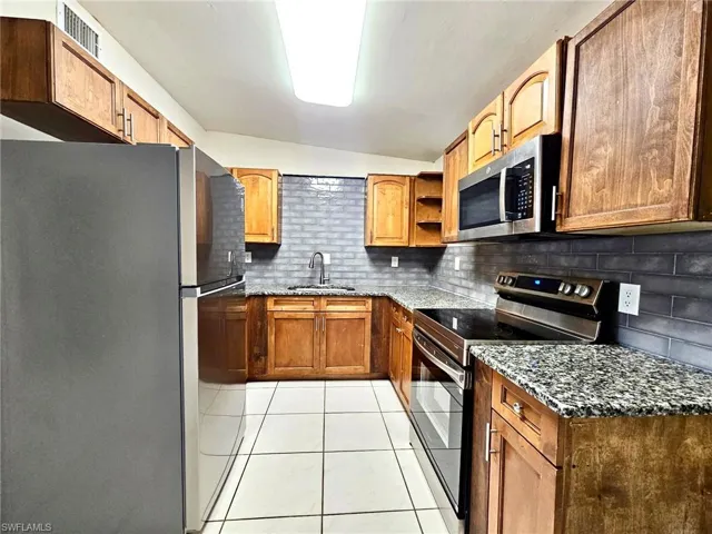 Kitchen with stainless steel appliances, dark stone counters, open shelves, lofted ceiling, and light tile patterned floors