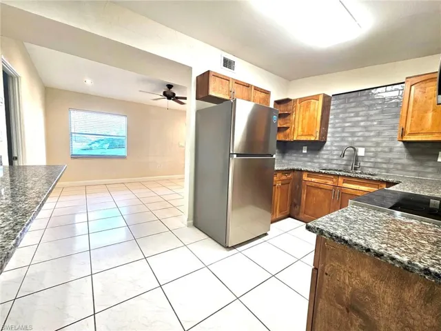 Kitchen with dark stone counters, freestanding refrigerator, open shelves, wood finish cabinets, and ceiling fan