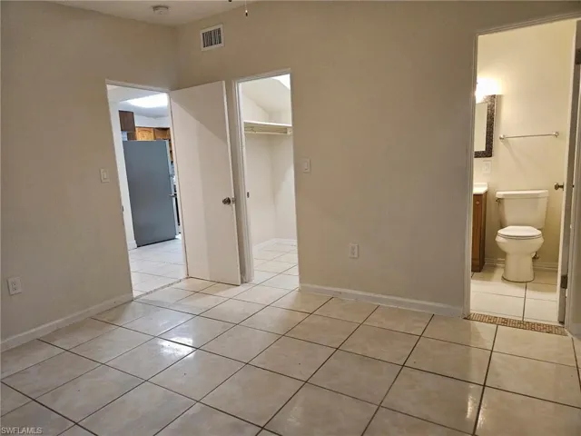 Unfurnished bedroom with light tile patterned flooring, freestanding refrigerator, and a walk in closet