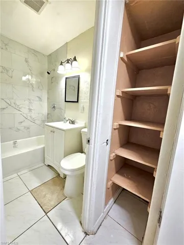 Bathroom with vanity, light marble finish flooring, shower / washtub combination, and a closet