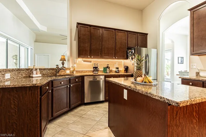 Kitchen with arched walkways, dark stone counters, appliances with stainless steel finishes, a peninsula, and a kitchen island