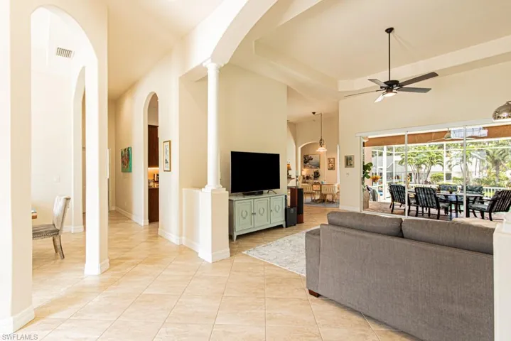 Living room with arched walkways, light tile patterned floors, ceiling fan, and a tray ceiling