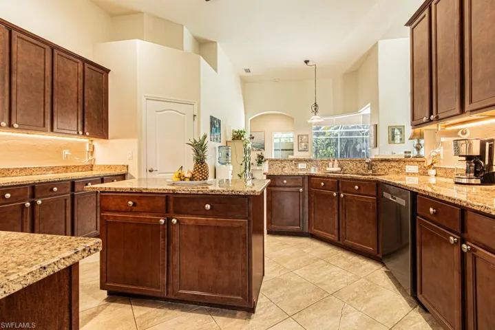 Kitchen featuring light stone counters, decorative light fixtures, a center island, stainless steel dishwasher, and light tile patterned floors