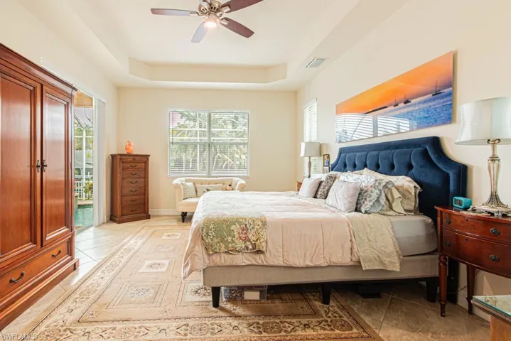Primary Bedroom with light tile patterned floors, seating area, tray ceiling, access to sunroom and 3 windows