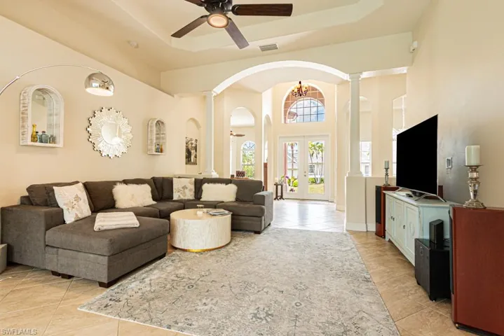 Living room with a tray ceiling, decorative columns, light tile patterned flooring, french doors, and a high ceiling