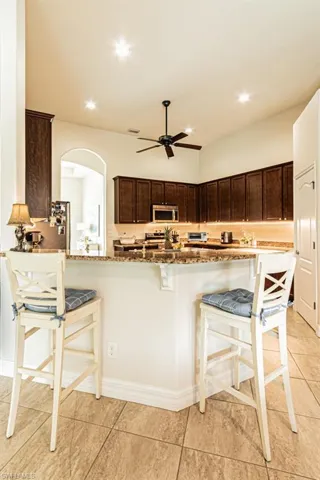Kitchen featuring a breakfast bar, dark brown cabinetry, dark stone countertops, recessed lighting, and light tile patterned flooring