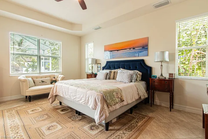 Primary Bedroom featuring a tray ceiling with fan, sitting area, 3 windows and light tile patterned flooring