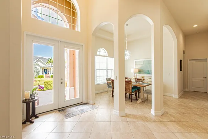 Foyer with arched walkways, french doors, light tile patterned flooring, and a high ceiling