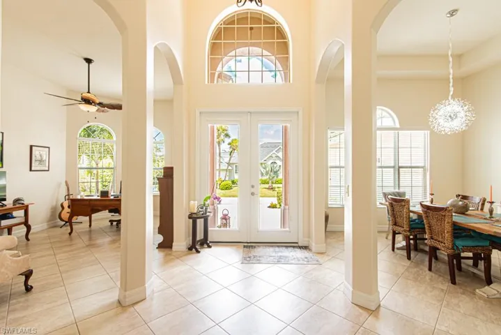 Entryway with french doors, arched walkways, light tile patterned floors, a chandelier, and a towering ceiling